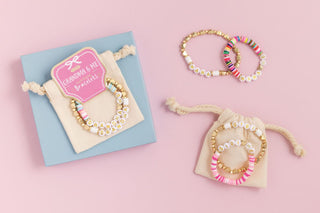 Set of beaded bracelets on a pink background with a blue card and pink label.