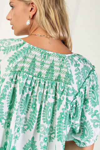 Green and white patterned blouse worn by a person on a plain background