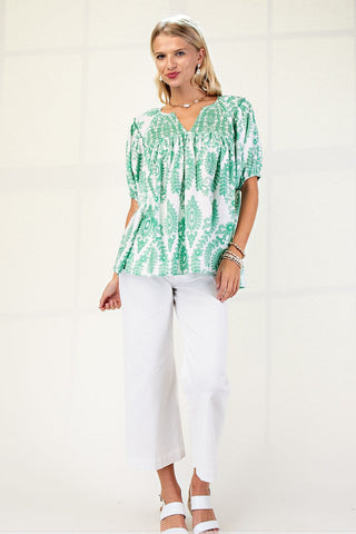 Woman wearing a green patterned blouse and white pants on a white background