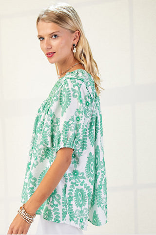 Woman wearing a green and white patterned blouse on a plain background