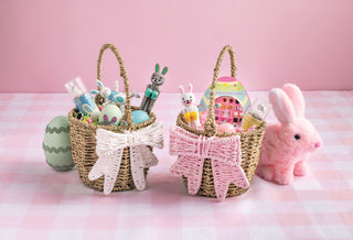 Two wicker Easter baskets with decorative items on a pink and white checkered tablecloth.