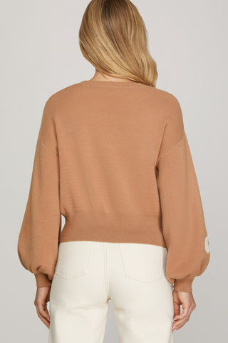 Woman wearing a taupe sweater with white floral patterns on a plain background