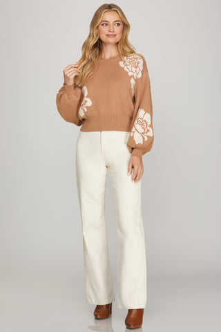 Woman wearing a taupe sweater with white floral patterns on a plain background