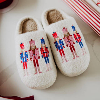 Pair of white slippers with nutcracker design on a light surface.