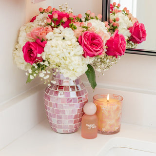 Bouquet of pink and white flowers in a mosaic vase on a bathroom counter with a lit candle.