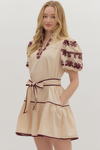 Woman wearing a beige dress with red floral embroidery on a white background