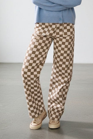 Woman wearing a light blue sweater and checkered pants standing in a minimalistic room.