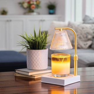 Table lamp with a glass candle holder on a wooden table, with a plant and books in the background.