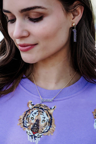 Woman wearing a purple sweatshirt with a decorative design, necklace, and earrings.
