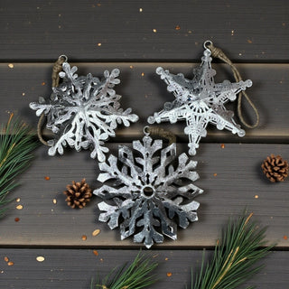 Decorative silver snowflake ornaments on a wooden surface with pine branches and cones.