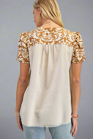 Woman wearing a beige and brown patterned top against a gray background