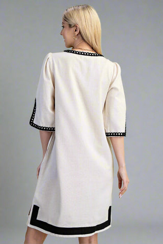 Woman wearing a white dress with black trim on a gray background