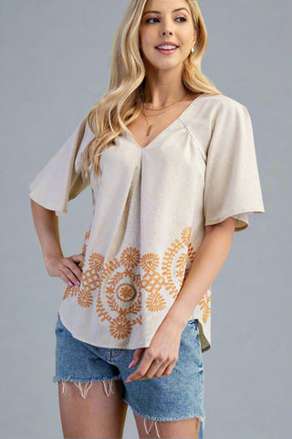 Woman wearing a beige blouse with floral patterns and denim shorts on a gray background