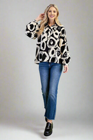 Woman wearing a black and white patterned blouse with blue jeans on a gray background