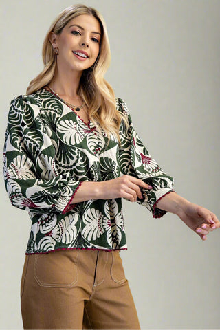 Woman wearing a patterned blouse with rolled-up sleeves on a plain background