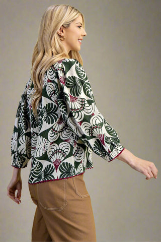 Woman wearing a patterned shirt and brown pants on a plain background