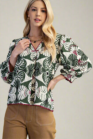 Woman wearing a patterned blouse with long sleeves on a plain background