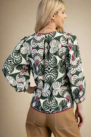 Woman wearing a patterned blouse with long sleeves on a beige background