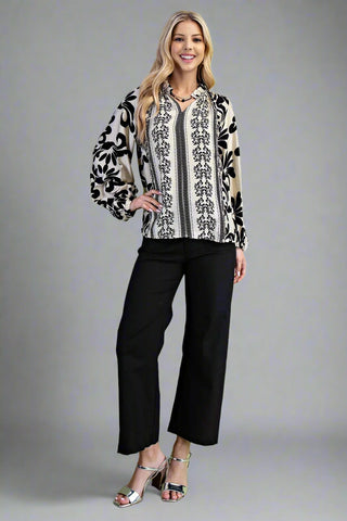 Woman wearing a patterned blouse and black pants on a gray background