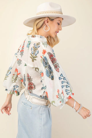 Woman wearing a floral embroidered blouse with a beige hat and light blue jeans on a beige background
