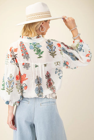 Woman wearing a floral embroidered blouse and wide-brimmed hat against a beige background