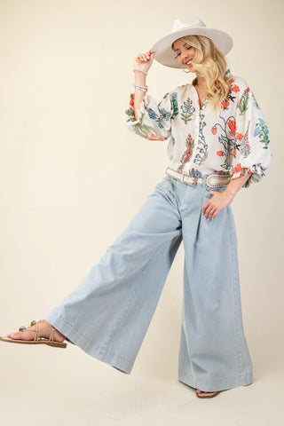 Woman wearing a floral blouse and light blue jeans with a white hat on a beige background