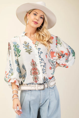 Woman wearing a floral blouse, white hat, and light blue jeans on a plain background