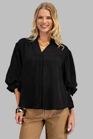 Woman wearing a black blouse and beige pants against a light green background