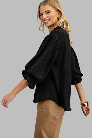 Woman wearing a black blouse with ruffled sleeves against a light green background