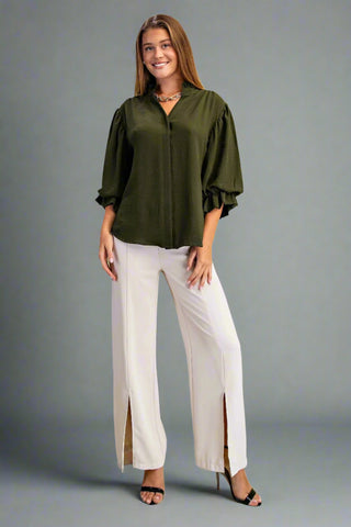 Woman wearing an olive green blouse and white pants on a light green background