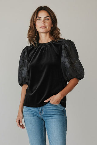 Woman wearing a black top with puff sleeves and blue jeans on a plain background
