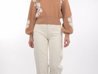 Video of a Woman wearing a taupe sweater with white floral patterns on a plain background